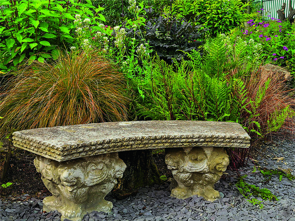 Изысканная скамья в классическом стиле эффектно отделяет цветник с декоративными травами от засыпанной серым сланцем дорожки.